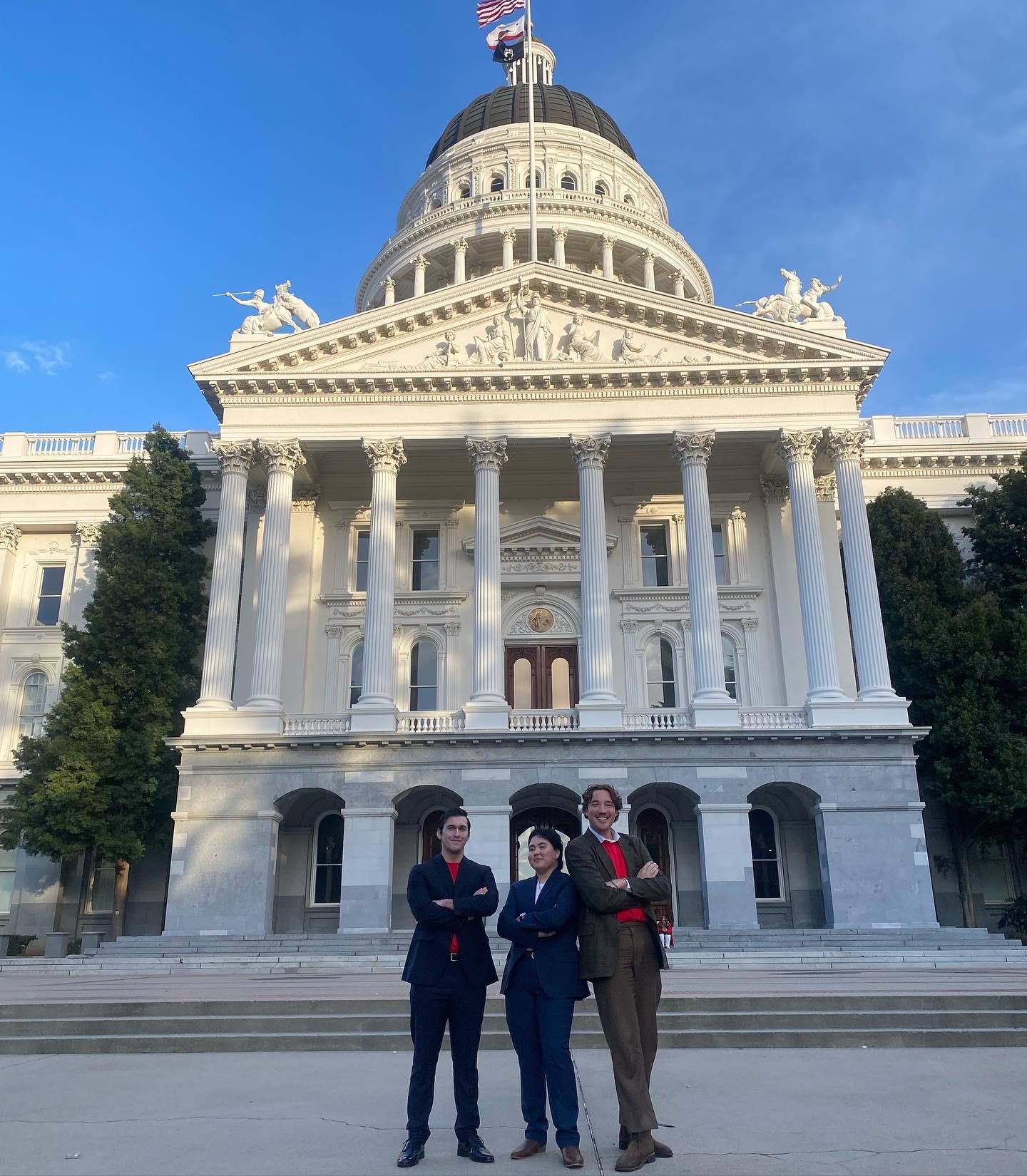 Three students stand in front of the State Capitol in Sacramento